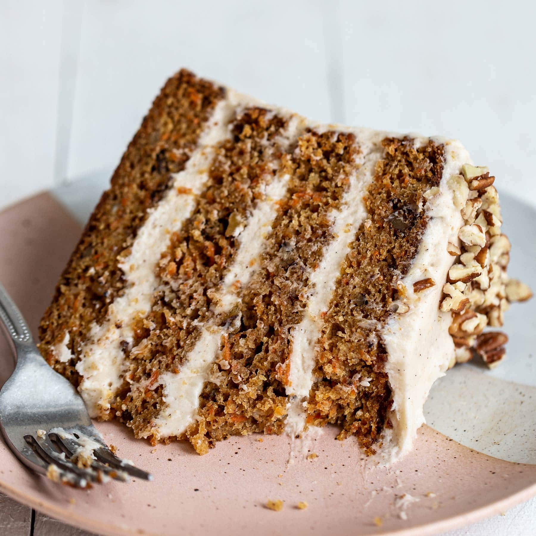 Slice of four layer brown butter carrot cake with cream cheese frosting on a plate with a forkful taken out