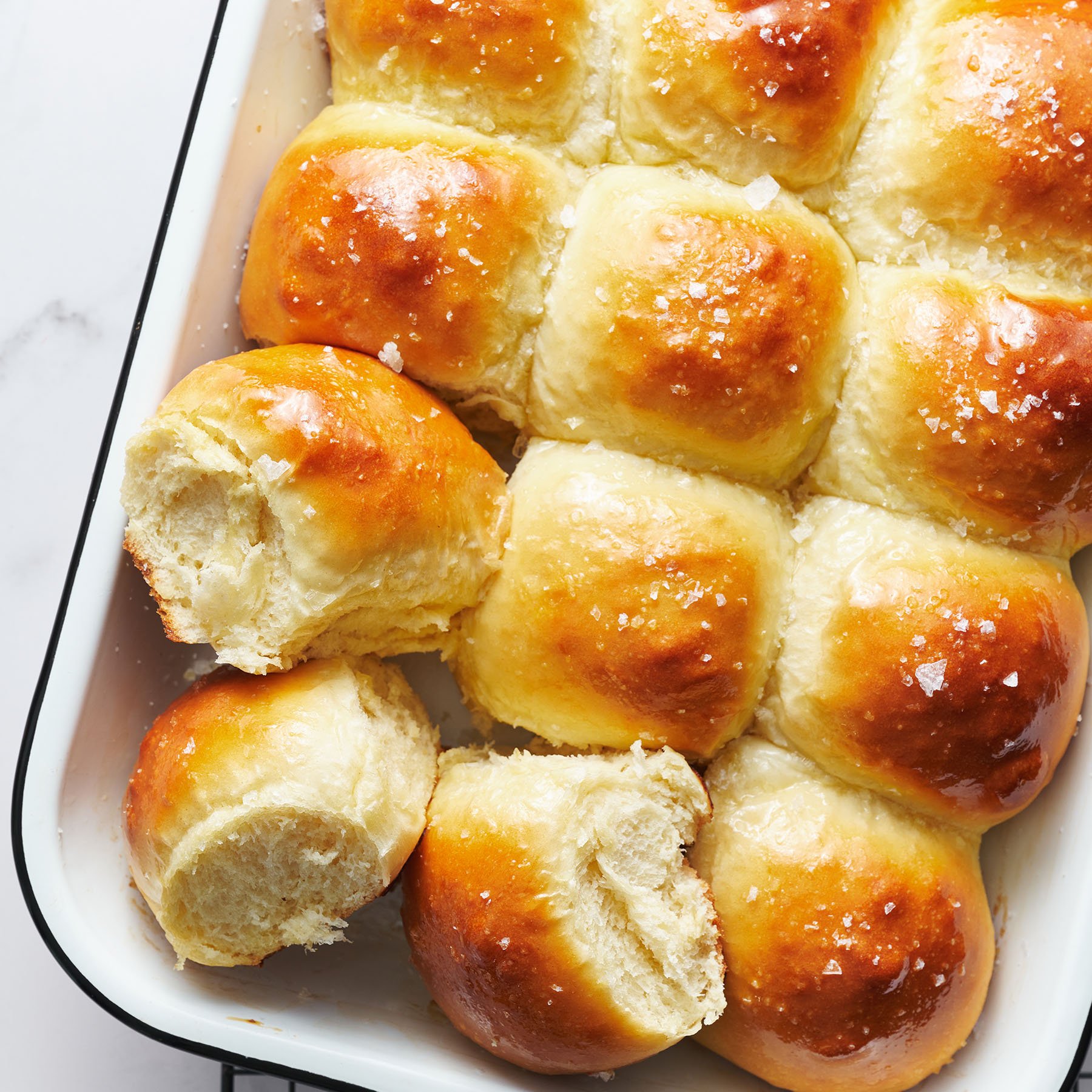 golden brown dinner rolls in a 9x13-inch baking pan, with some rolls on their sides to show the fluffy, soft interior.