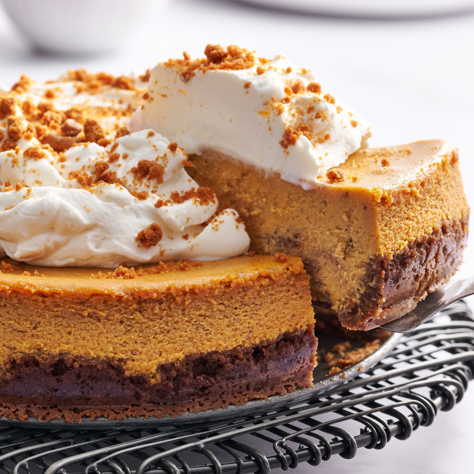 pumpkin cheesecake topped with whipped cream with a slice being removed to serve