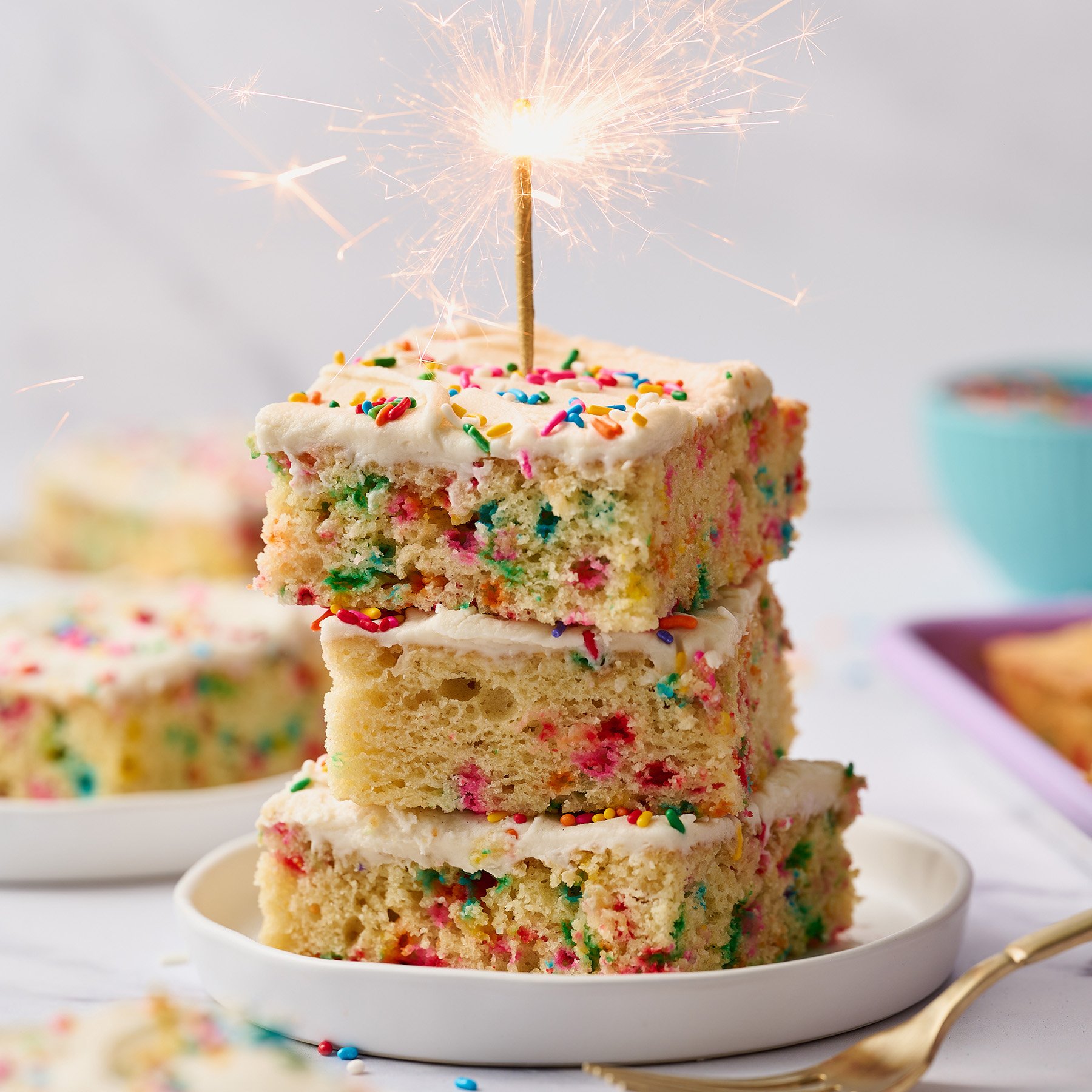 stack of three funfetti cake slices with a birthday sparkler candle lit on top