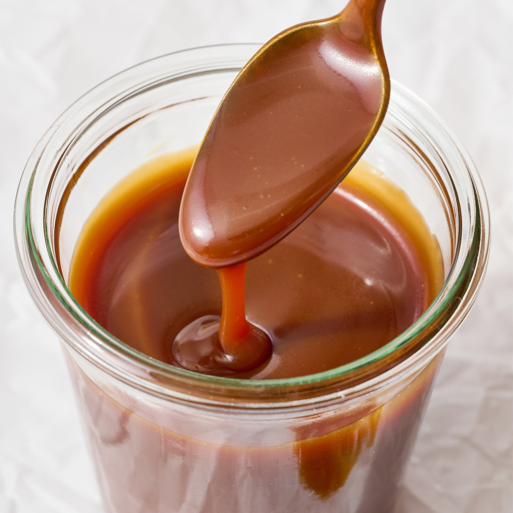 homemade salted caramel sauce in a jar with a spoon drizzling