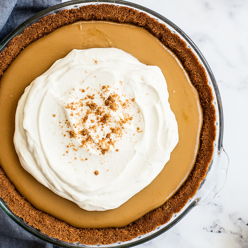 a whole butterscotch pudding pie topped with fresh whipped cream and a sprinkling of ground up speculoos cookies