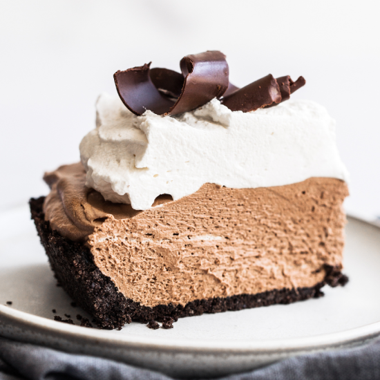 a perfect slice of French silk pie with whipped cream and chocolate curls on top, on a plate, ready to serve.