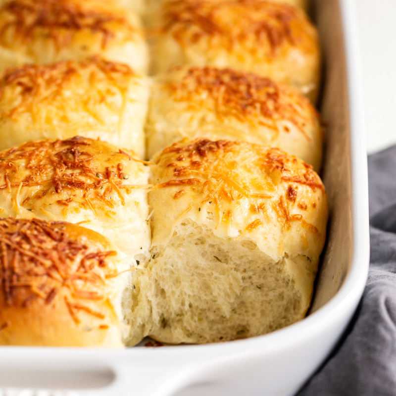 garlic herb cheese rolls in a ceramic baking pan, with a roll removed so you can see their soft interior.